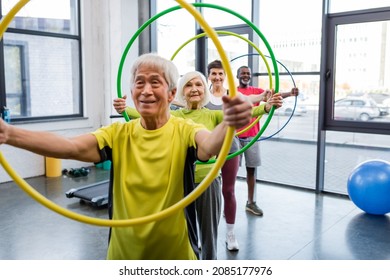 Positive interracial people holding hula hoops and looking at camera in gym - Powered by Shutterstock