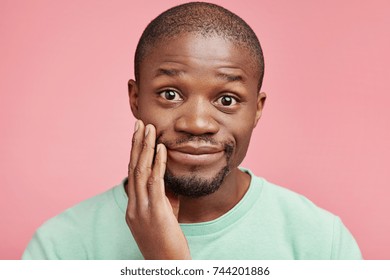 Positive joyful delightful dark skinned male keeps hand on cheek, looks with dark warm eyes into camera, expresses gratitude, has good relationships with girlfriend or relatives. Ethnicity concept