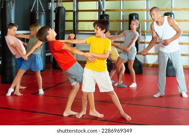 Positive kids in pair exercising self-defense movements during group class with male coach