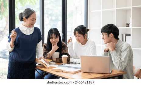 A positive and kind senior Asian female teacher is teaching her students in the classroom. A group of a university students studying with a mature female professor. education concept - Powered by Shutterstock