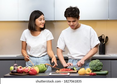 Positive Korean Husband And Wife Preparing Healthy Dinner Cooking Together In Kitchen Indoors. Asian Family Making Salad Cutting Vegetables, Having Romantic Date At Home On Weekend.