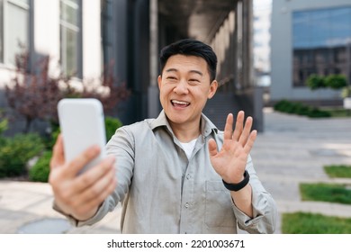 Positive Korean Man Using Smartphone Making Video Call, Walking In The City Outside, Waving Hello To Cellphone. Distant Online Communication Concept