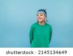 Positive lady with colored hair and in a green sweater stands on a blue background and looks away and laughs.