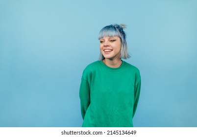 Positive lady with colored hair and in a green sweater stands on a blue background and looks away and laughs. - Powered by Shutterstock