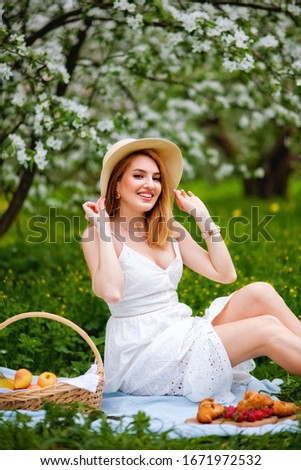 A positive lady in a hat and sundress laughs against the background of a blooming Apple tree. An optimistic woman in a wide smile in the garden. Spring time