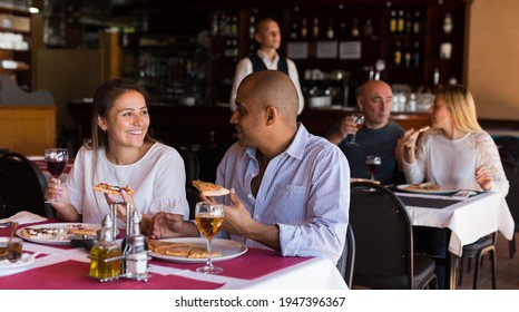 Positive Latin American Married Couple Sitting In Cozy Restaurant And Eating Pizza With Wine