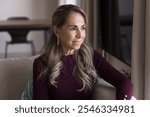 Positive Latin retired mature woman looking away with good thoughts, sitting on home couch, daydreaming, thinking on retirement, wellness, healthcare, smiling, enjoying homey leisure