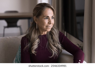 Positive Latin retired mature woman looking away with good thoughts, sitting on home couch, daydreaming, thinking on retirement, wellness, healthcare, smiling, enjoying homey leisure - Powered by Shutterstock