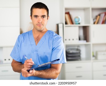 Positive Latino Doctor With Folder Of Documents At Clinic Office