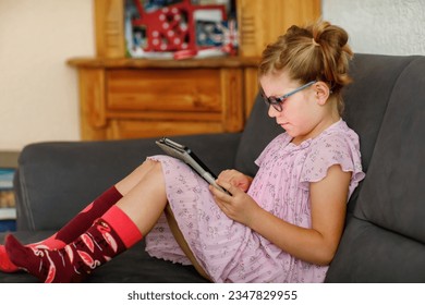 Positive little girl, holding tablet computer in her hands. Preschool child with eyeglasses playing games and learning with different apps. - Powered by Shutterstock