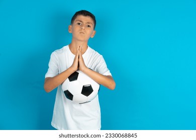 Positive Little hispanic boy wearing white T-shirt smiles happily, glad to receive pleasant news from interlocutor, keeps palms together, People emotions concept.