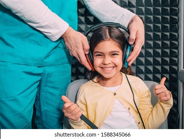 Positive Little Mixed Race Child Wearing Headphones Showing Thumbs Up While Hearing Exam.audiometry Test