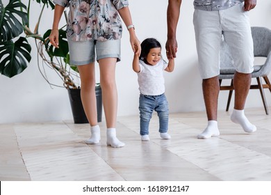 Positive little one and half year mixed-time girl walks around house and takes her first steps holding hands of father and mother in cozy home. Concept of care of love and support for next generation - Powered by Shutterstock