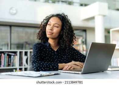 Positive Lovely African American Girl, Office Worker, Sales Manager, Corporate Marketer, Sit At Work Desk In Modern Office, Looking Away, Planning Strategy, Thinking Project, Dreaming About Vacation
