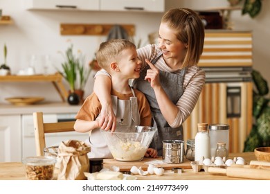 Positive loving family: mother smearing nose of son with flour while making dough together at wooden table in kitchen - Shutterstock ID 2149773499