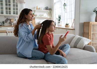 Positive loving mother spending time with teen daughter at home, smiling young woman mom braiding long hair of teenage girl child before school in morning. Family weekend, Mother-daughter date concept - Powered by Shutterstock