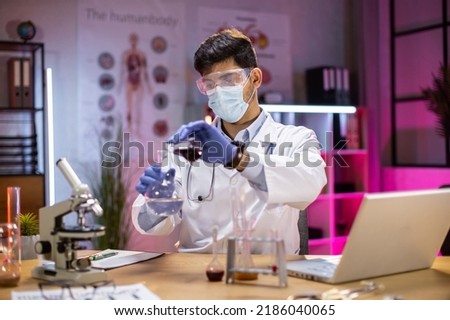 Positive male arab scientist or medical in lab coat holding test tube with reagent, laboratory glassware containing chemical liquid. Microscope, Biochemistry laboratory research.