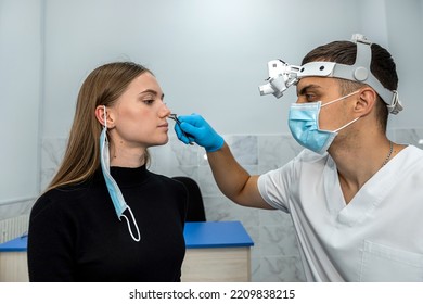 Positive Male Otorhinolaryngologist Is Checking Nose With Otoscope Of His Patient Girl In Hospital. Nasal Congestion. A Patient In A Modern ENT Clinic. The Concept Of Otolaryngology.