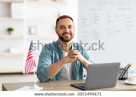 Positive male teacher giving English lesson online, using laptop at home office. Young Caucasian tutor explaining grammar rules to students on web indoors. Modern remote education concept