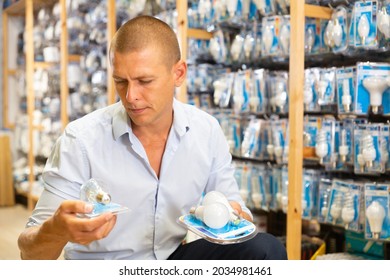 Positive man chooses new bulbs in lighting shop - Shutterstock ID 2034981461