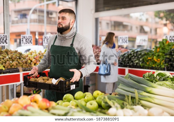 Positive man employee showing box with kiwi in\
grocery shop. High quality\
photo