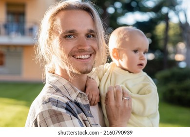 Positive Man Holding Blurred Baby And Looking At Camera Outdoors