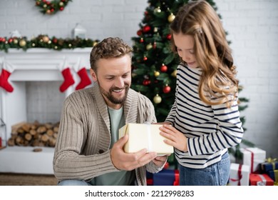 Positive Man In Knitted Cardigan Holding Gift Box Near Child During Christmas At Home