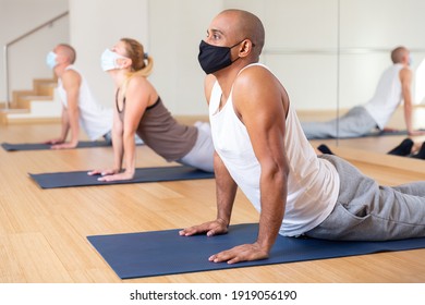 Positive Man In Protective Mask Practicing Yoga Lesson At Group Class, Maintaining Healthy Lifestyle During Coronavirus Pandemic