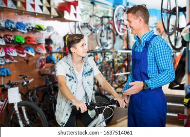 Positive Man Seller In Uniform Helping Teenage Boy Choose Bicycle In Sport Store