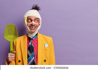 Positive Man With Shiner Under Eye, Has Missing Teeth, Beaten By Someone, Forgets About His Health Problems, Holds Strainer, Looks Aside, Notices Someting Funny, Poses Over Purple Wall, Blank Space