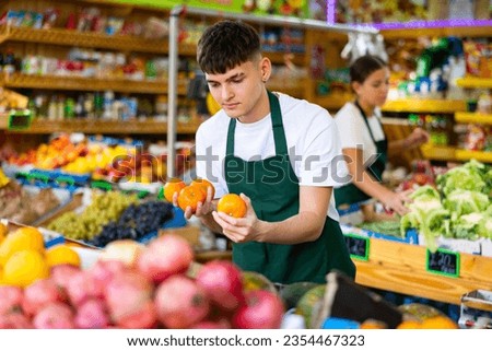 Positive man store employee displaying assortment of oranges at fruit department in supermarket