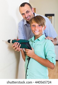 Positive man teaching son to using electric drill wall at home