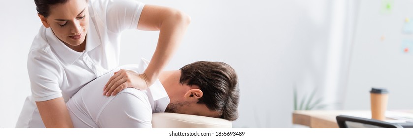 Positive masseur doing arm massage for client in office on blurred background, banner