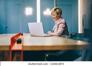 Positive Mature Coach Laughing During Watching Business Webinar Online On Modern Laptop Connected To Wireless 4G Internet.Cheerful Female Entrepreneur 50 Years Old Reading Funny News On Netbook