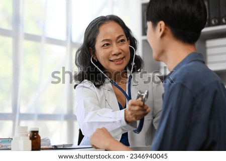 Positive mature doctor using stethoscope, listening to male patient breath or heartbeat. Healthy care concept.