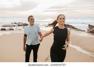 Positive mature european woman holding man hand, enjoy workout together in morning on sea beach, outdoor. Motivated for sports, fitness and body care, teamwork and active lifestyle - Shutterstock ID 2310519737