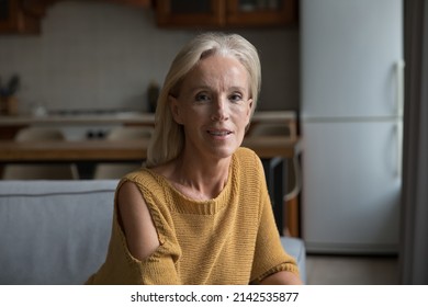 Positive Mature Lady Home Head Shot Portrait. Blonde Middle Aged Pensioner, Homeowner, Retired Woman In Casual Sitting On Couch In Living Room, Looking At Camera, Smiling