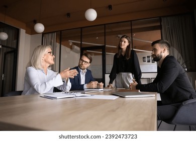 Positive mature project manager sharing creative ideas for project on brainstorming, speaking to listening colleagues, young female leader. Business team meeting low angle shot - Powered by Shutterstock