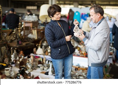 Positive Mature Spouses Buying Retro Handicrafts On Indoor Flea Market