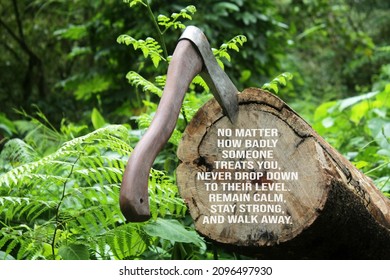 Positive Message Sign In The Log With Axe. - No Matter How Badly Someone Treats You, Never Drop Down To Their Level. Remain Calm, Stay Strong, And Walk Away. An Axe On Wood On Green Forest Background.