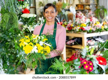 Positive mexican female florist in apron holding composition from natural flowers at flower shop