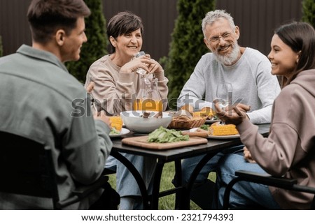 Positive middle aged parents looking at blurred children near summer food during barbeque party and parents day celebration at backyard in june, cherishing family bonds concept