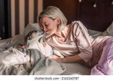 Positive Middle Aged Relaxed Woman With Dog Lying Down And Staying At Home, Daydreaming, Napping, Looking Away, Enjoying Day Off In Bed