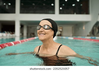 positive middle aged woman in swim cap and goggles swimming in pool, water, recreation center, spa - Powered by Shutterstock