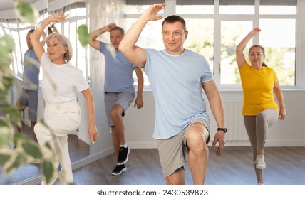 Positive middle-aged male instructor leading energetic zumba class for group of seniors in mirrored fitness studio.. - Powered by Shutterstock