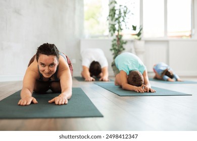 Positive middle-aged woman practicing child's pose of yoga on black mat together with her family - Powered by Shutterstock