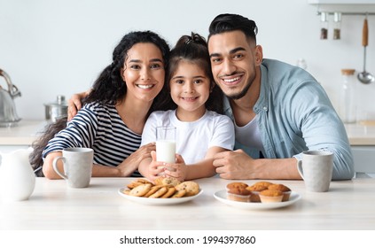 Positive Middle-eastern Family Of Three Father, Mother And Little Daughter Enjoying Breakfast Together At Cozy Kitchen, Sitting At Table, Drinking Coffee, Milk And Eating Fresh Home-made Pastry