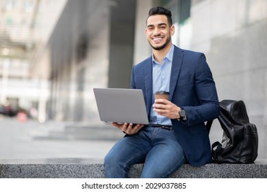 Positive middle-eastern guy in formal clothes sitting by business center building with laptop, having coffee break while conference, IT manager arab man getting ready for business meeting, copy space - Shutterstock ID 2029037885