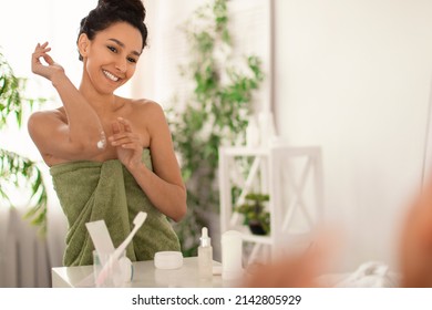 Positive Millennial Woman In Towel Applying Soothing Cream At Elbow, Moisturizing Dry Skin In Front Of Mirror At Home, Free Space. Pretty Young Female Pampering Herself At Bathroom