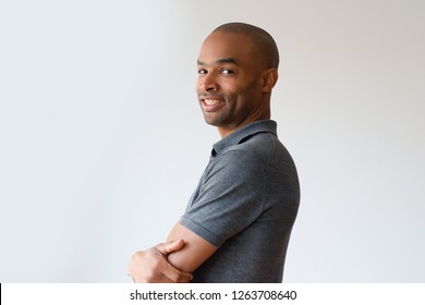 Positive mix raced guy posing with arms folded. Side view of young black man turning face to camera and smiling. Side portrait concept